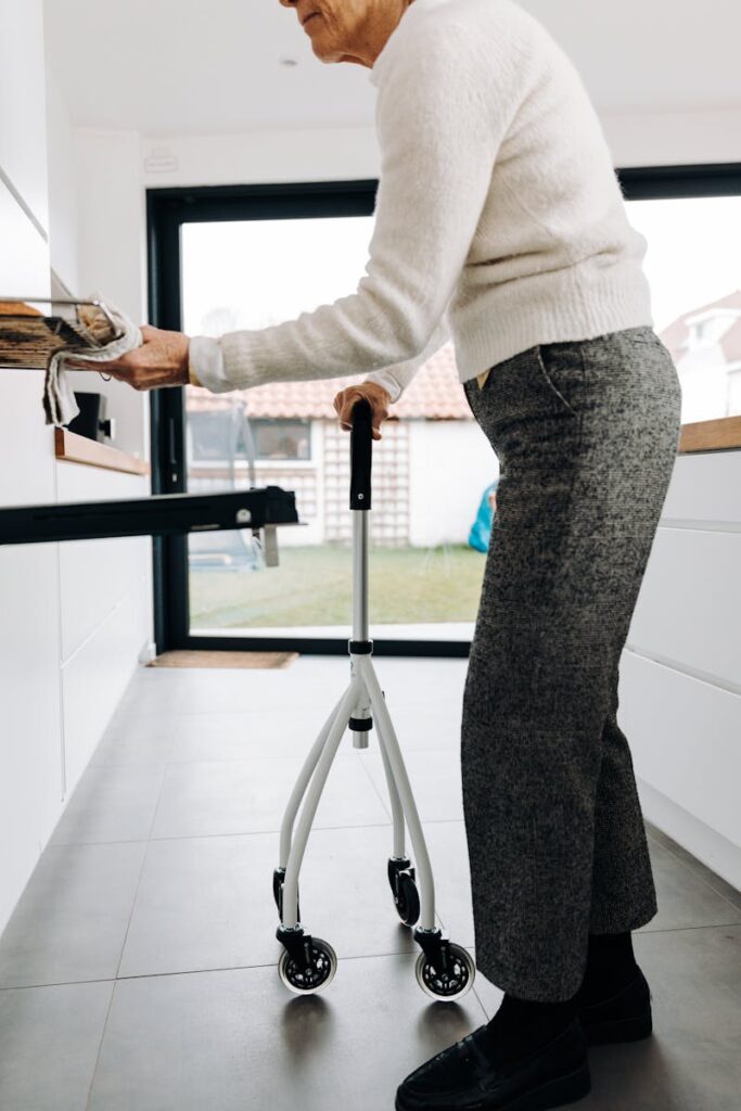 Elderly woman using a walker to assist with mobility in a bright, modern kitchen setting.